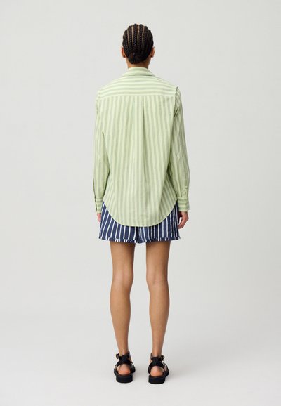 Camicia button-up a righe verticali verde chiaro con orlo curvo, abbinata a pantaloni corti blu navy con righe orizzontali.