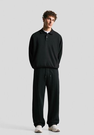 Black athletic outfit featuring a long-sleeve polo with a collar and button, loose-fit pants with drawstring, and light-colored shoes.