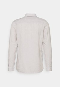 Vue arrière d'une chemise beige clair à manches longues avec de fines rayures verticales et poignets boutonnés sur un fond uni.