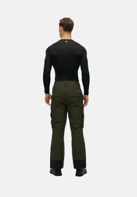 Zwarte langemouwen shirt en olijfgroene cargobroek met meerdere zakken, voorzien van een zwarte onderzoom en stevige zwarte schoenen.