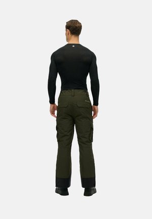 Schwarzes Langarmshirt und olivgrüne Cargo-Hosen mit mehreren Taschen, mit einem schwarzen unteren Saum und robustem schwarzen Schuhwerk.