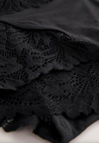 Svart tyg med intrikat spetskant. Spetsen visar blommönster med genombrutna detaljer, vilket kontrasterar mot den släta texturen på det underliggande materialet.