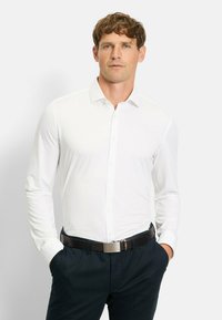 Weißes Langarmhemd mit Slim-Fit und klassischem Kragen. Kombiniert mit dunkelblauen Hosen und einem dunklen Gürtel. Glatte Textur.