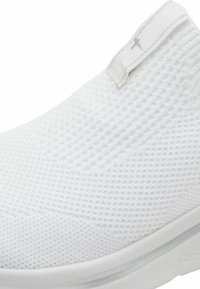 Baskets blanches à enfiler avec une tige en maille texturée, un col rembourré et une semelle en caoutchouc lisse. Design minimaliste sans logo visible.