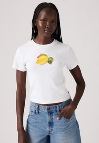 Tricou alb din bumbac, cu un grafic mare de lămâie galbenă și frunze verzi, cu mâneci scurte și un design ajustat. Purtați-l cu blugi albaștri.