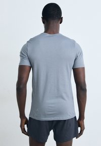 T-shirt cinza claro de mangas curtas com uma textura suave e um design ajustado, usado com calções escuros, visto de trás.