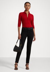 Red ribbed long-sleeve polo shirt, black high-waisted jeans, black woven belt, holding a small black handbag, and wearing black strappy sandals.