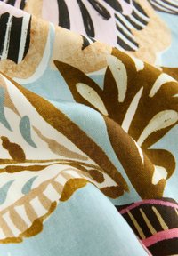 Patterned fabric featuring floral designs in brown, pink, and black on a light blue background. Smooth texture with a soft drape.