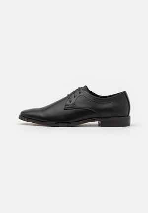 Chaussure habillée en cuir noir avec un bout pointu, un design à lacets et une texture lisse. Présente des coutures discrètes et un talon bas et plat.