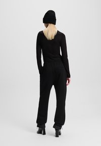 Schwarzes Langarmshirt und schwarze Jogginghose mit elastischem Bund und einer hinteren Tasche. Kombiniert mit schwarzen Absatzstiefeln und einer Mütze.