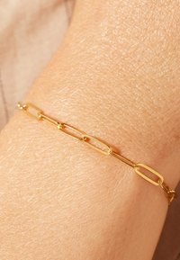 Gold chain bracelet featuring elongated, linked ovals with a smooth finish, resting on a textured skin surface.