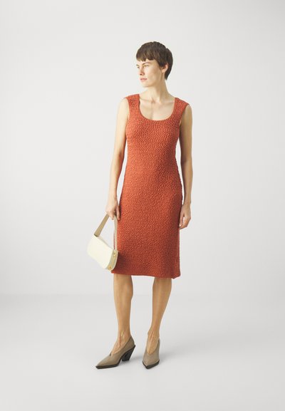 Rochie texturată portocalie cu decolteu rotund, asociată cu o geantă de umăr crem și pantofi cu toc pătrat în nuanță taupe. Design simplu, ajustat.