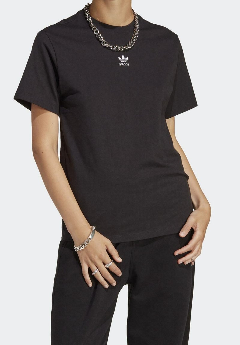 Svart bomullströja med korta ärmar, med en liten vit Adidas-logga på bröstet. Kombinerad med matchande svarta byxor och silveraccessoarer.