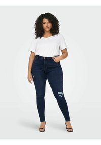 Mörkblå högmidjade skinny jeans med slitna detaljer och en vit kortärmad V-ringad t-shirt. Slät tyg, tight passform.