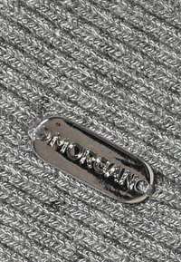Etiqueta de metal plateado con "MORGAN" grabado, unida a un fondo de tela texturizada de color gris claro con un patrón anudado.