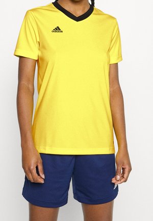 Person wearing a yellow Adidas short-sleeve sports shirt with black collar and navy blue athletic shorts.