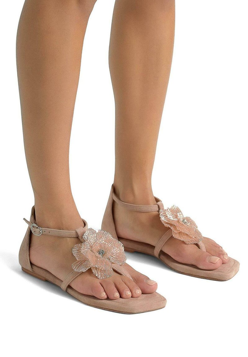 Sandali in suede rosa chiaro con cinturino alla caviglia, dotati di un accento di fiore decorato con perline e suola piatta. Il design open-toe mette in risalto le dita dei piedi.