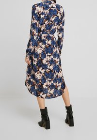 Lång blommig klänning i blå och rosa nyanser, med långa ärmar, bälte i midjan, rund nederkant och ihop med svarta stövletter.