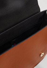 Sac en cuir marron avec une texture lisse, doté d'une fermeture magnétique et d'un intérieur en tissu noir, comprenant une poche zippée et des emplacements pour cartes.