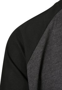 Kortärmad T-shirt med en design i svart och mörkgrå färgblock, tillverkad av mjuk bomull med en slät textur och raglanärmar.