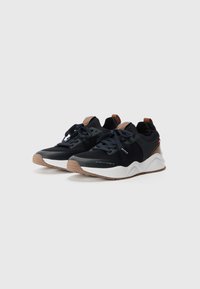 Black athletic shoes with a knit upper, leather accents, and a white, textured sole. Laces are dark, featuring subtle logo details on the side.