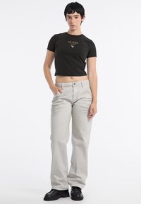 Czarny krótki T-shirt z złotym logo "GUESS", jasnoszare proste spodnie i czarne masywne botki. Prosty, dopasowany krój.