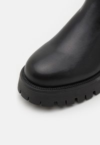 Bota de tobillo de cuero negro con puntera redondeada, acabado texturizado y suela de goma gruesa y estriada. Sin hardware ni acentos visibles.