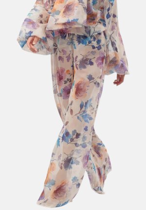 Donna con pantaloni floreali trasparenti e larghi e top coordinato con ampie maniche a campana in colori pastello delicati.