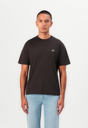 Black cotton t-shirt with a round neckline and short sleeves. Features a small green Lacoste logo on the upper left chest area.