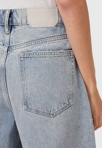 Jeans in denim blu chiaro con una patch in pelle sul cinturino e una singola tasca posteriore con dettagli di cucitura sottili.