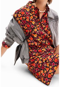 Kwiatowa sukienka w czerwonym, pomarańczowym i żółtym kolorze na czarnym tle, w połączeniu z jasnoszarym dżinsowym kurtką. Posiada luźny krój i krótkie rękawy.