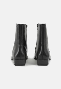 Schwarze Lederknöchelboots mit glatter Oberfläche, ausgestattet mit einem kleinen Blockabsatz und Reißverschlüssen an der Rückseite. Minimalistisches Design ohne Muster.