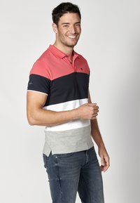 Férfi polo ing piros, tengerészkék, fehér és szürke vízszintes csíkokkal, pamutból készült, két gombos gallérral és rövid ujjakkal.