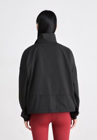 Schwarze, leichte Windbreaker-Jacke mit hohem Kragen und fallenden Schultern, ausgestattet mit elastischen Bündchen und einem lässigen Schnitt.