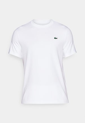 Valkoinen lyhythihainen t-paita, joka on valmistettu puuvillasta; vasemmassa rinnassa vihreä brodeeratun krokotiilin logo; sileä pinta.