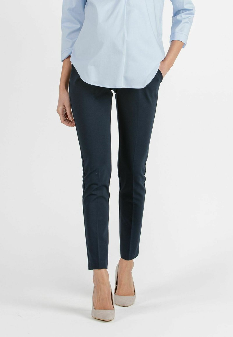 Donkerblauwe op maat gemaakte broek met een slim fit, gemaakt van een gladde stof. Gecombineerd met een lichtblauw overhemd met knopen en beige puntige hakken.