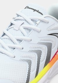 Fehér sportcipő texturált felső résszel, fekete és szürke részletekkel, fényvisszaverő elemekkel, valamint egy színes talppal, amelyen sárga és rózsaszín gradiens található.