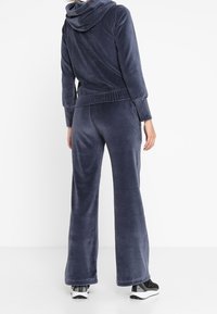 Dunkelblauer Velours-Trainingsanzug mit einer Kapuzenjacke, gerippten Bündchen und weit geschnittenen Hosen. Weicher Stoff mit lässigem Schnitt.