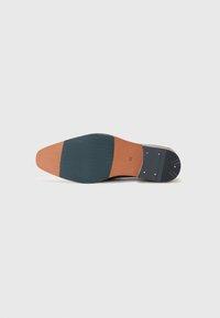 Talpa de pantof din piele maro cu intersolă bej. Cureaua din cauciuc verde închis prezintă un model în zigzag. Include iti metalice și mărimea 42.