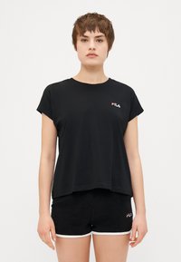 Melnas īsām piedurknēm T-krekls ar apaļu kakla izgriezumu, izgatavots no kokvilnas, ar sarkanu un baltu FILA logo uz krūtīm. Saskaņots ar melniem šortiem, kuriem ir baltas akcenti.