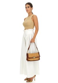 Borsa intrecciata marrone con una chiusura dorata, abbinata a un crop top beige a costine e pantaloni bianchi a vita alta, tenuta con una mano.