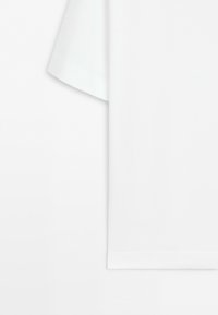 Close-up of the white short sleeve and hem of a plain white T-shirt, shown against a white background.