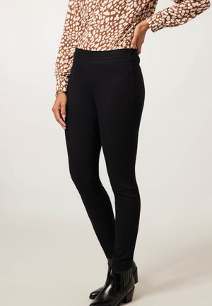 Zwarte slim-fit broek van rekbare stof, met een gladde textuur en een elastische tailleband, gestyled met zwarte enkellaarsjes.