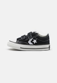 Sorte kanvas sneakers med hvit gummisåle og tåhette, med to borrelåser og et hvitt stjernemotiv på siden.