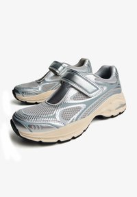 Pantofi sport cu un upper din plasă metalică argintie, curea ajustabilă și tălpi din cauciuc bej, evidențiind detalii texturate și stilistice.