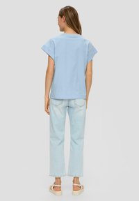 Lichtblauwe katoenen t-shirt met korte dolmanmouwen, relaxed fit, gecombineerd met lichtgewicht rechte jeans en beige platform sandalen.