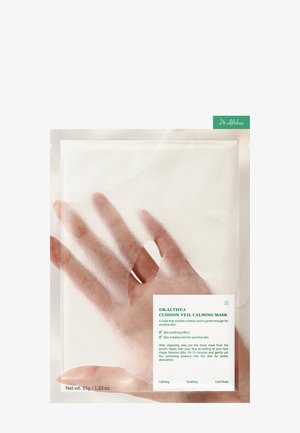 Main tenant une pochette translucide du masque apaisant Dr. Althea Cushion Veil avec les détails du produit et les instructions sur un fond blanc.