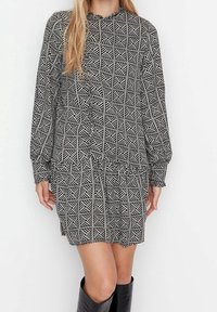 Schwarz-weißer gemusterter Kleid mit langen Ärmeln, geraffter Taille und rundem Halsausschnitt. Besitzt ein geometrisches Design mit diagonalen Streifen.
