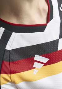 Maglia sportiva caratterizzata da strisce orizzontali in nero, rosso e giallo. Realizzata in tessuto testurizzato con scollatura rossa a contrasto e dettagli geometrici.
