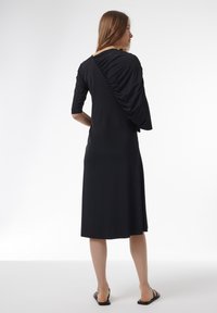 Vestido negro hecho de una tela suave, con un diseño fruncido en la parte posterior y mangas hasta el codo, que presenta una silueta fluida hasta la rodilla.